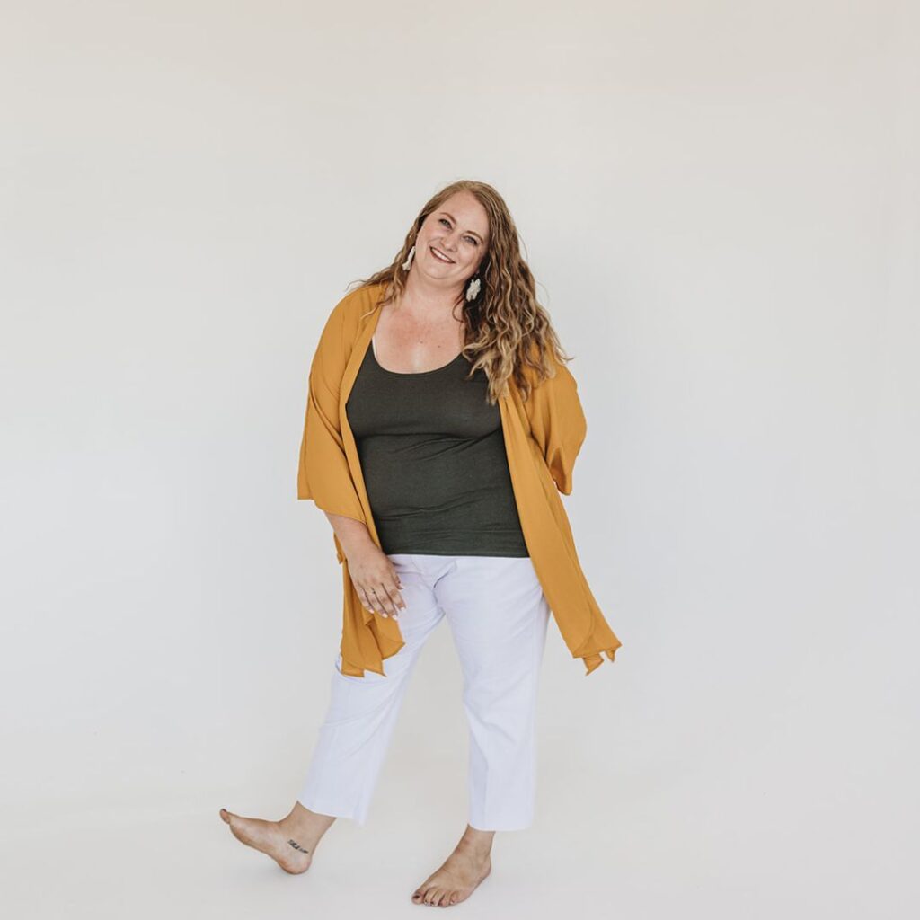 Photo of owner and founder of Mills and Mae Services Brianne Price in a yellow cardigan, green t-shirt, white pants, no shoes