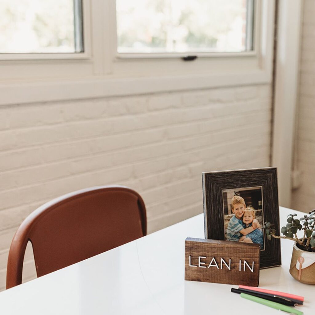 Big windows. Pens on a table A sign that says Lean In, a photo of Brianne Price's kids, and a plant